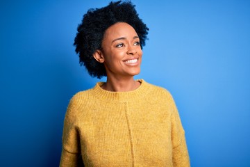 Fototapeta na wymiar Young beautiful African American afro woman with curly hair wearing yellow casual sweater looking away to side with smile on face, natural expression. Laughing confident.