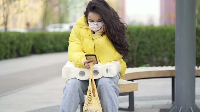 No emotional woman sitting on the bench with shopping stuff, wearing face mask. Slowmotion.