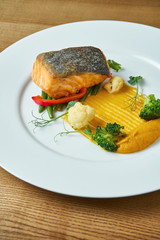 Appetizing grilled salmon steak with a side dish of yellow puree, fresh asparagus, broccoli and cauliflower on a white plate. Healthy and tasty food
