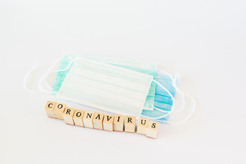 Word coronavirus written with wooden blocks with black letters isolated with a protective surgical mask