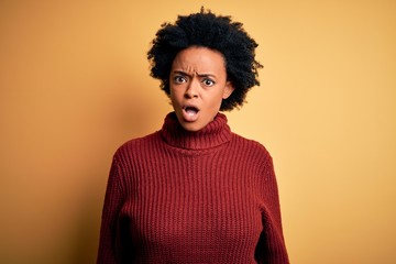 Obraz na płótnie Canvas Young beautiful African American afro woman with curly hair wearing casual turtleneck sweater In shock face, looking skeptical and sarcastic, surprised with open mouth