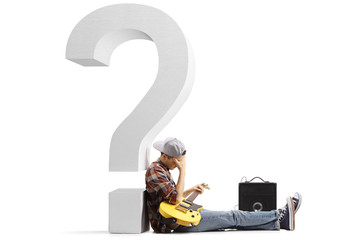 Sad young man sitting on the floor with a guitar and leaning on a big question mark