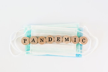 Word pandemic written with wooden blocks with black letters laying on protective disposable surgical masks