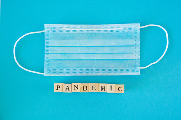 Word pandemic written with wooden blocks with black letters laying on protective disposable surgical masks