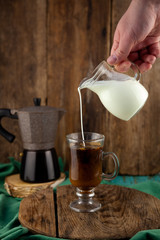 Milk is poured into decanter coffee. Geyser coffee maker, creamer on a wooden table. Glass cup with...