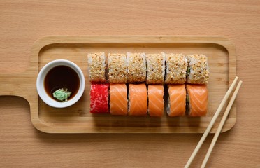 Sushi rolls, soy sauce, wasabi and chopsticks on a wooden tray.