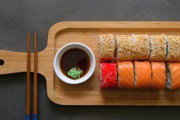 Sushi rolls, soy sauce, wasabi and chopsticks on a wooden tray.