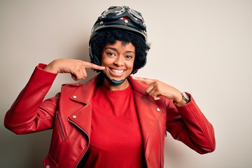 Young African American afro motorcyclist woman with curly hair wearing motorcycle helmet smiling cheerful showing and pointing with fingers teeth and mouth. Dental health concept.