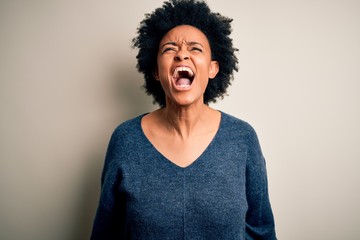 Young beautiful African American afro woman with curly hair wearing casual sweater angry and mad screaming frustrated and furious, shouting with anger. Rage and aggressive concept.