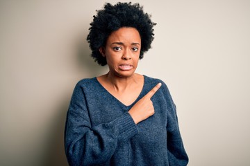 Young beautiful African American afro woman with curly hair wearing casual sweater Pointing aside worried and nervous with forefinger, concerned and surprised expression