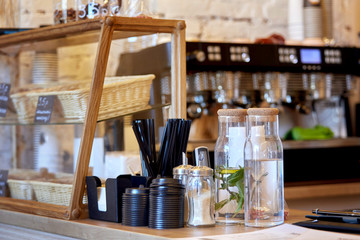Lids for coffee, straws, sugar, water with natural herbs, mint, in a cafe near the shop window with food.