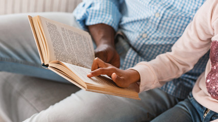 Stay home activities. Lillte African American girl reading fairy tale with her granddad, close up of hands holding book