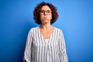 Fototapeta na wymiar Middle age beautiful curly hair woman wearing casual striped shirt over isolated background puffing cheeks with funny face. Mouth inflated with air, crazy expression.