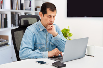 Cropped shot of a handsome young businessman sitting in his home office and looking contemplative while working on his laptop