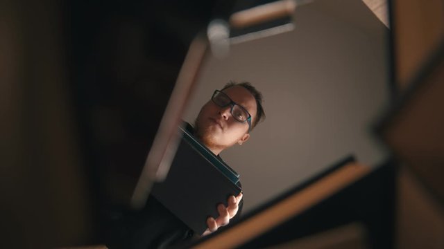 A young man in glasses looking in the gap around the books and putting the book in it