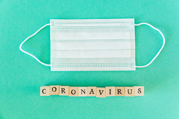 Word coronavirus written with wooden blocks with black letters isolated with a protective surgical mask
