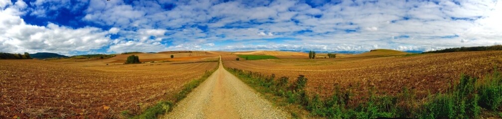 Dirt Road Passing Through Field Against Cloudy Sky