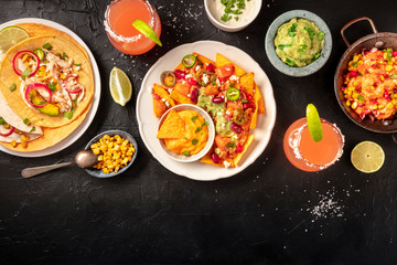 Mexican food, a flat lay on a dark background with a place for text. Nachos, tortillas, Paloma cocktails, guacamole and other dishes, overhead shot