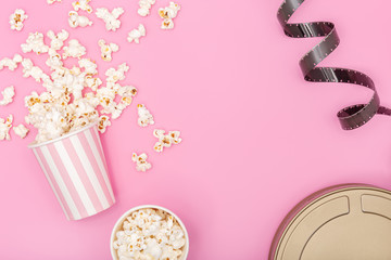 Popcorn bucket, film strip and film can on pink background. Movie or TV background. Top view Copy space