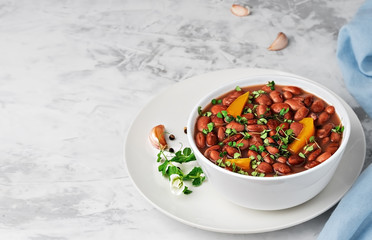 Closeup of a cup with boiled red beans decorated with basil leaves. Healthy vegetarian dish, next to a bowl of spices, and bread. Close-up on a dark vintage background, horizontal view with copy space