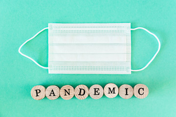 Word pandemic written with wooden blocks with black letters laying on protective disposable surgical masks