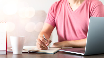 Man's hand using pen writing on the notebook on the wood table with technology equipment device while remote working.