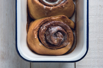 Close-up of baking pan with fresh homemade cinnamon rolls, over a white rustic wooden table.