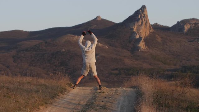 man performs exercise on country road amid mountains in sunset