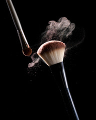 Make-up brush with pastel pink cosmetic powder spreading on black background