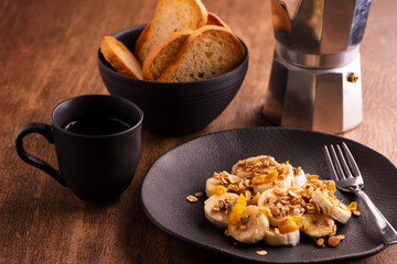 plate with sliced banana with granola, candied fruit and honey, toast and a cup of coffee