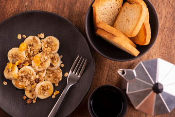 plate with sliced banana, granola, candied fruit and honey, toast and a cup of coffee