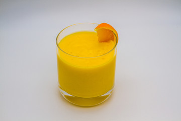 Glass of yellow mango fruit shake with slice of orange with neutral background