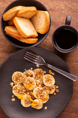 plate with sliced banana and granola with dried fruit, toast and a cup of coffee