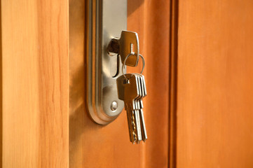 Metal key from the bunch of keys inserted into the lock of the wooden door. Warm colors, close up