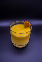 Isolated glass of yellow mango fruit shake with slice of orange with black and dark purple background (vertical)