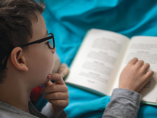 Little child, 8 years old boy reading a book at home with his toy teddy bear