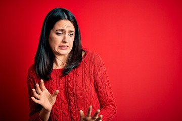 Young brunette woman with blue eyes wearing casual sweater over isolated red background disgusted...
