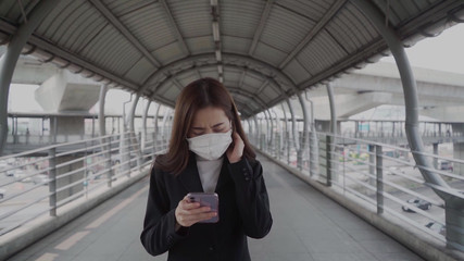 Asian businesswoman wears black formulas and wears a mask Using a mobile phone and a smartphone while commuting to work During the Coronavirus epidemic
