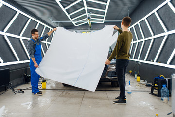 Workers holds hood template of car protection film