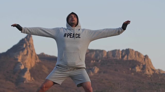 Young man of athletic physique share gymnastic exercises against the backdrop of mountains at sunset