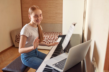 Teenage girl musician plays the digital piano during an online class using a laptop at home. Education, technology, hobby and self-isolation project