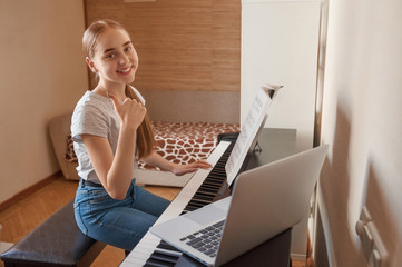 Smile teenage girl showing thumbs up during online piano class using laptop at home. Education, technology, hobby and self-isolation project