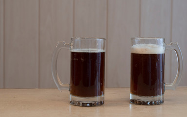 Two glass mugs with dark and beer on the table.