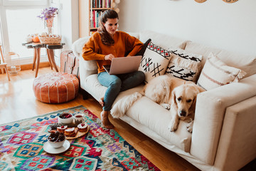 .Young freelance woman working from home with her laptop accompanied by her faithful golden...