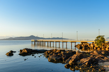tourist pier under blue sky in calm sea with rocks in the foreground and mountains on the horizon - 340933200