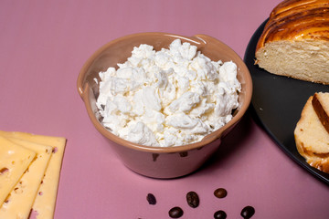 Cottage cheese, cheese and a bun for breakfast. The benefits and harms of cottage cheese for health. Healthy morning food. Background with the image of breakfast, a pleasant pink morning.