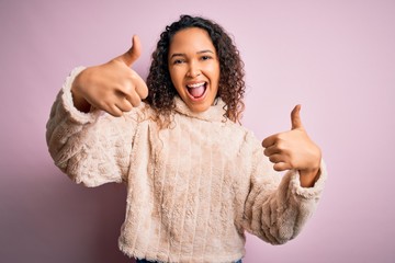 Young beautiful woman with curly hair wearing casual sweater standing over pink background...