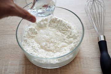 subjective view of hand pouring water over a glass container with flour, with a stirred veneer next to it