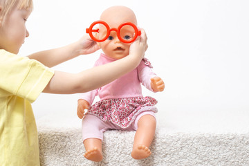 The child plays with a doll and puts on toy glasses. The concept of pediatric ophthalmology,...