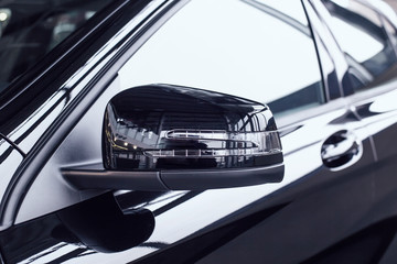 Modern beautiful side rear-view mirror in a new car with a built-in direction indicator. Black car at a car dealership, aerodynamic